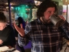 Lee shrugs and drinks w his mug at Porters' Pub (Pre-Covid).